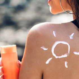 Woman wearing two piece bikini applying suncream with sun drawn on back on the tropical beach.Summer vacations