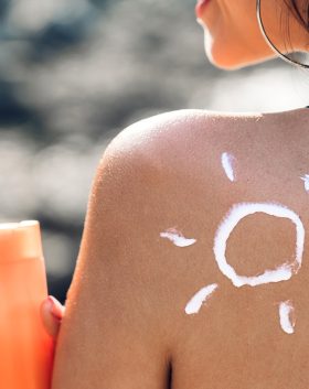 Woman wearing two piece bikini applying suncream with sun drawn on back on the tropical beach.Summer vacations