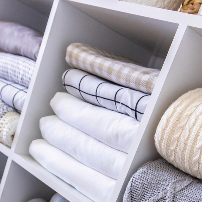 deco-bed-linens-neatly-folded-white-wooden-cupboard-shelves-with-potted-plants-scandi-minimalism