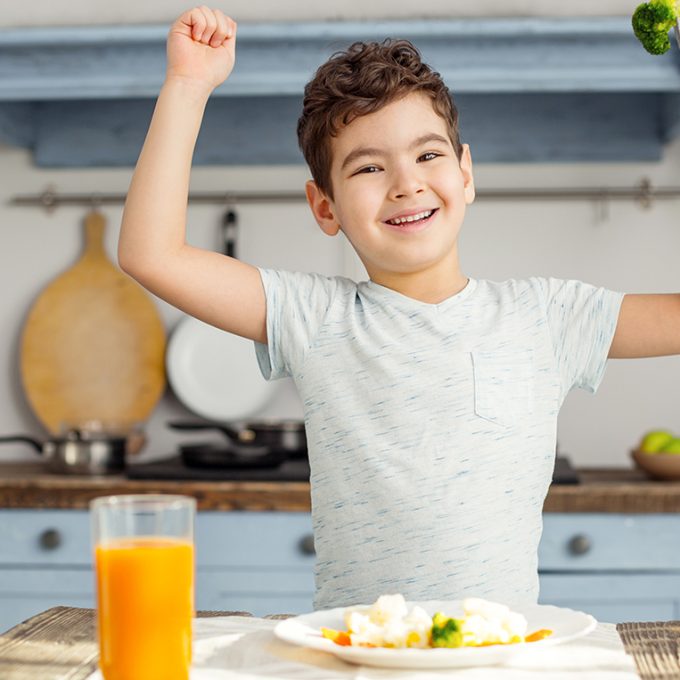 i-am-strong-handsome-cheerful-dark-haired-little-boy-having-healthy-breakfast-smiling-showing-his-muscles