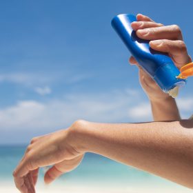 Woman applying sunscreen on her hands from a bottle on the beach with the sea in the background. SPF sunblock protection concept.selective focus
